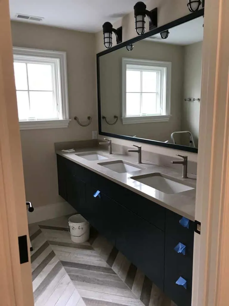 Double vanity with a white stone top and two undermount sinks on black cabinets, herringbone floor