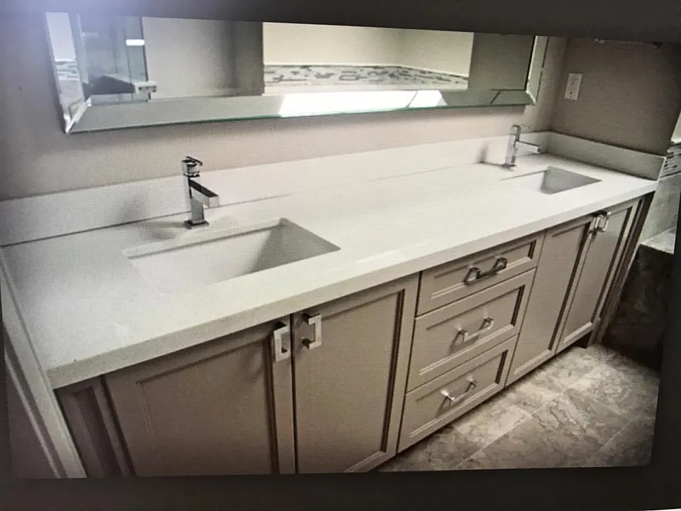 Long white vanity top with a sloped integrated sink cut into the stone, gray cabinets below