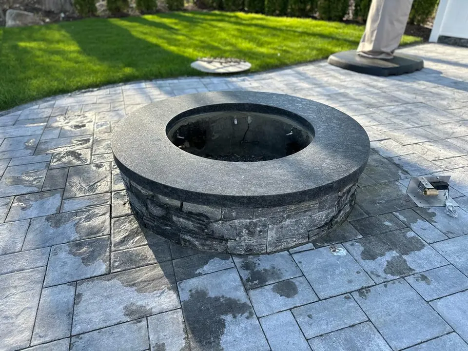 Round fire pit with a dark stone cap on a stacked-stone wall, on a paver patio