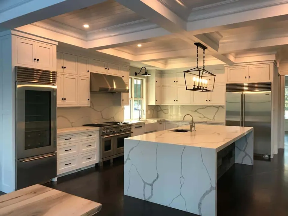 Kitchen island with waterfall ends in a white stone with bold gray veins, under a coffered ceiling, with a matching full-height backsplash behind the range