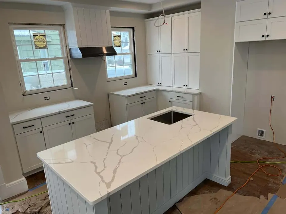 White island with soft gold and gray veins and an undermount sink, on a beadboard island base in a white kitchen