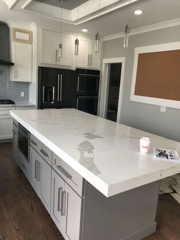Long white island with a thick built-up edge and gray veining over light gray cabinets