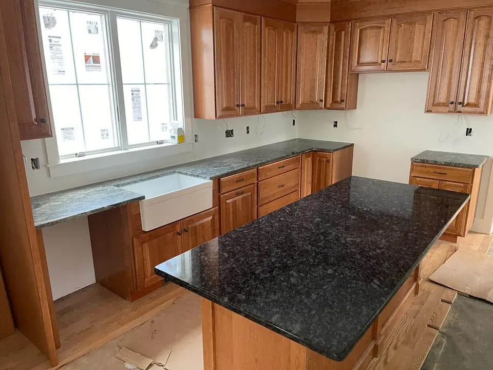 Black granite island and counters with warm wood cabinets and a white farmhouse sink