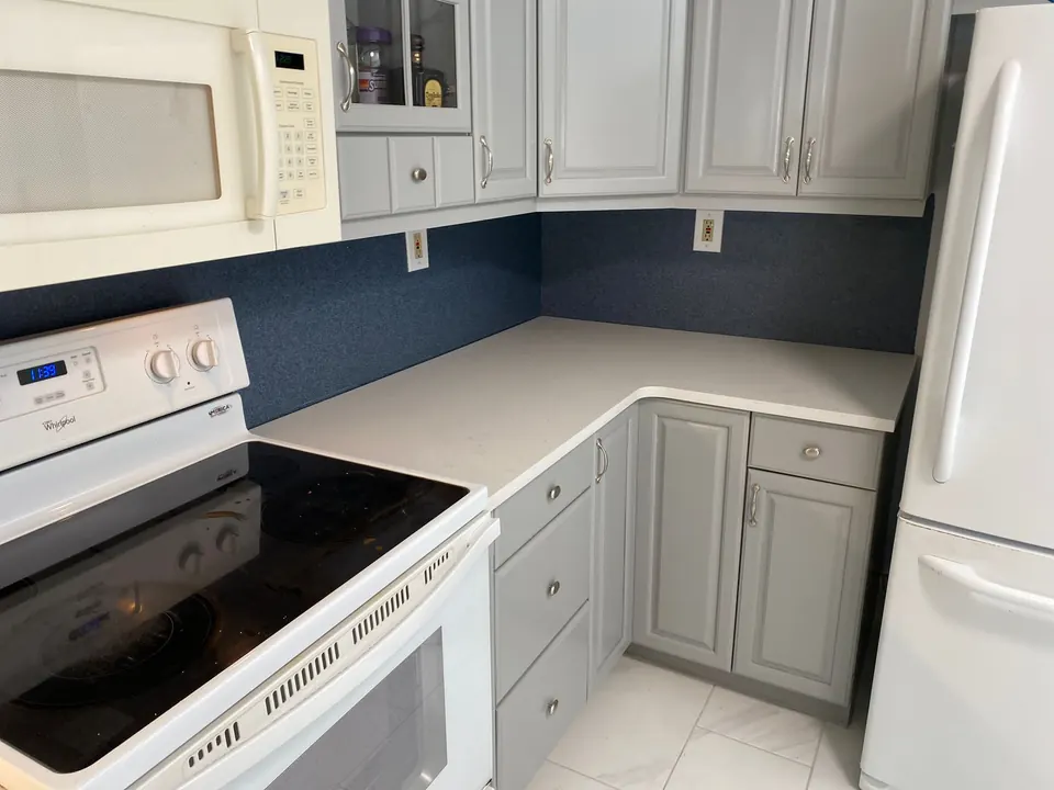 White quartz counters in an L-shaped kitchen with white appliances and a navy backsplash