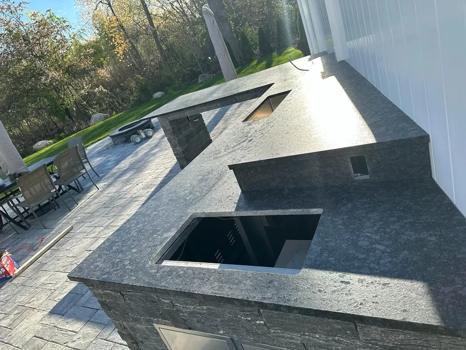 Close view of the outdoor kitchen: dark stone counter with an undermount sink and the bar beyond