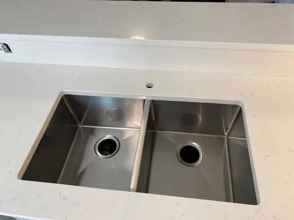 Close-up of a stainless double-bowl sink mounted under a white quartz counter