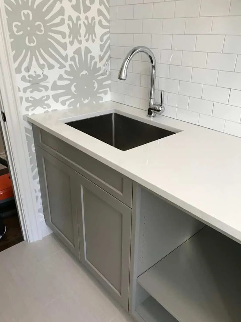 White counter with a single stainless undermount sink and a pull-down faucet against white subway tile