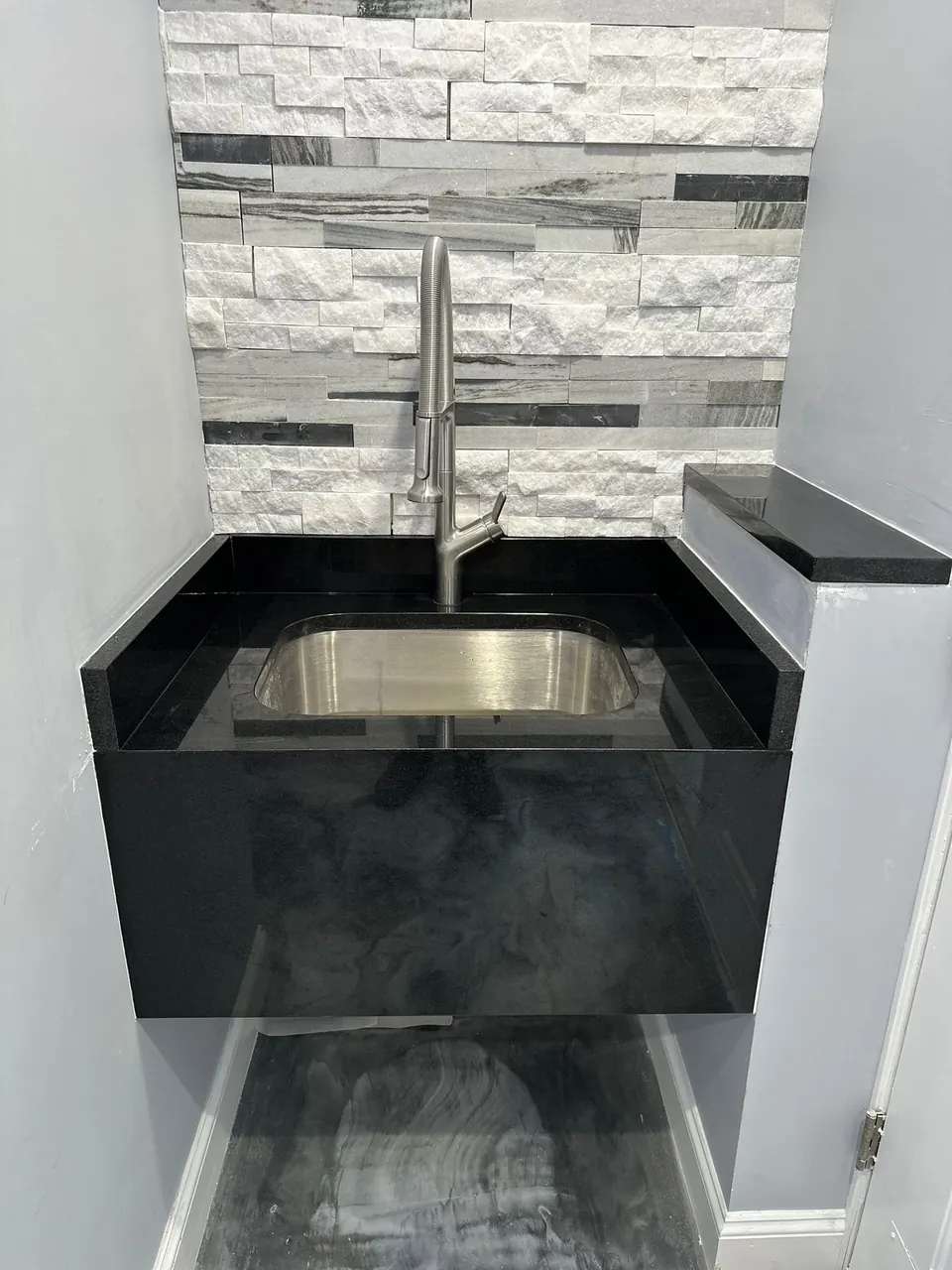 Black stone bar top and apron around a stainless sink, with a gray and white stacked-stone backsplash