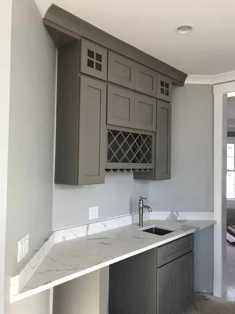 Corner wet bar with a white veined top cut on an angle, a small bar sink and gray cabinets with a wine rack